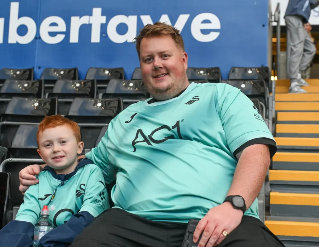 Father and young son in Swansea City shirts in the stand